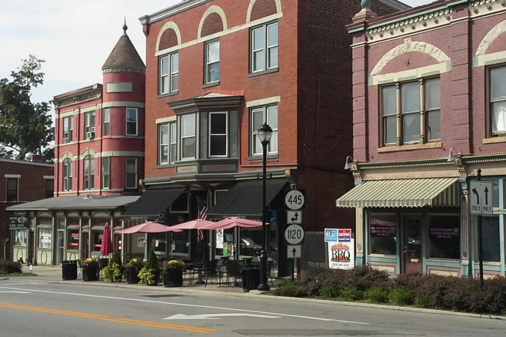 Fort-Thomas-Kentucky 1 | Helmer Somers Law Brick storefronts along a small-town street with outdoor cafe seating under pink umbrellas.