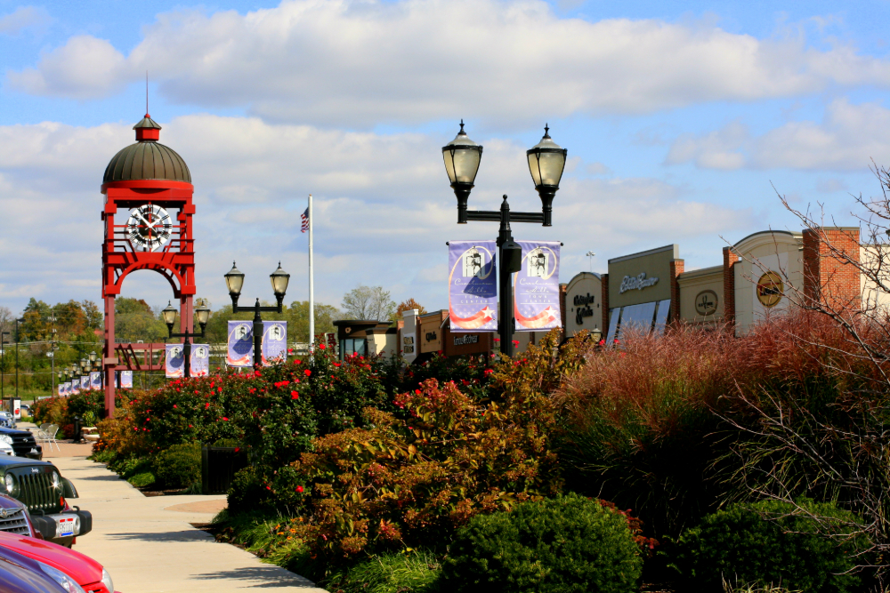 Red clock tower with a domed top along a shopping street, lined with banners, lamps, and storefronts.
