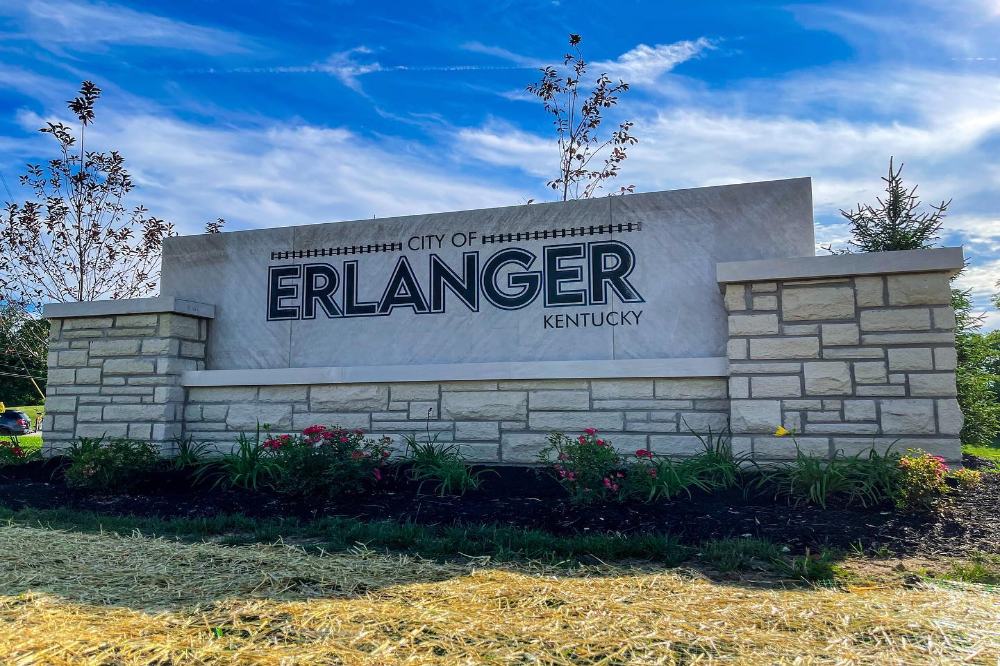 City of Erlanger, Kentucky sign on a stone wall with a landscaped flower bed and a blue sky above.