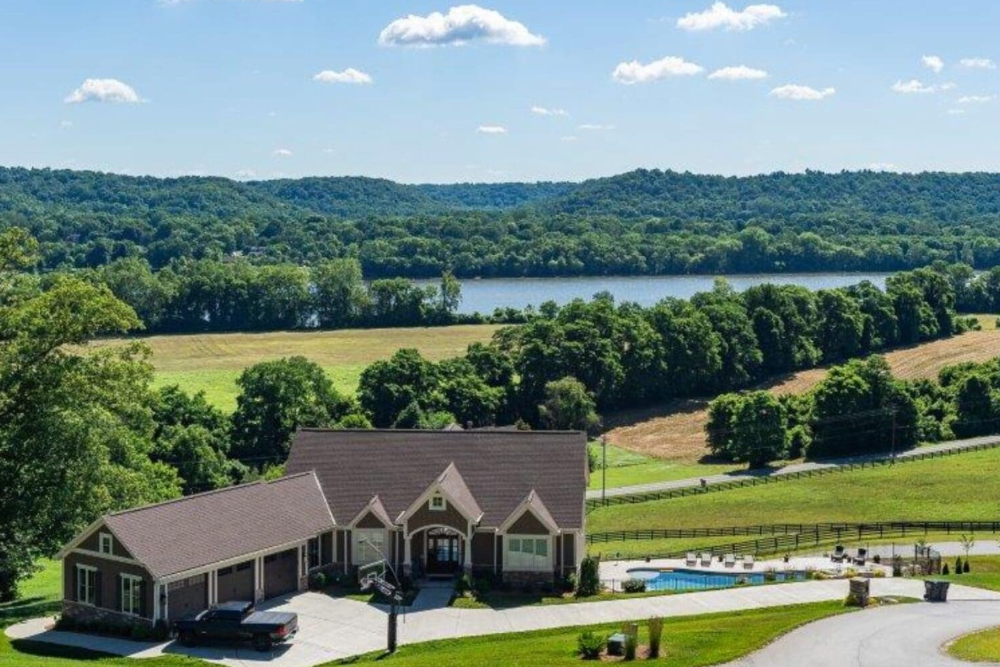 Hebron-Kentucky | Helmer Somers Law A house with a driveway and a swimming pool, set in a spacious green landscape with fields, trees, and a distant lake.