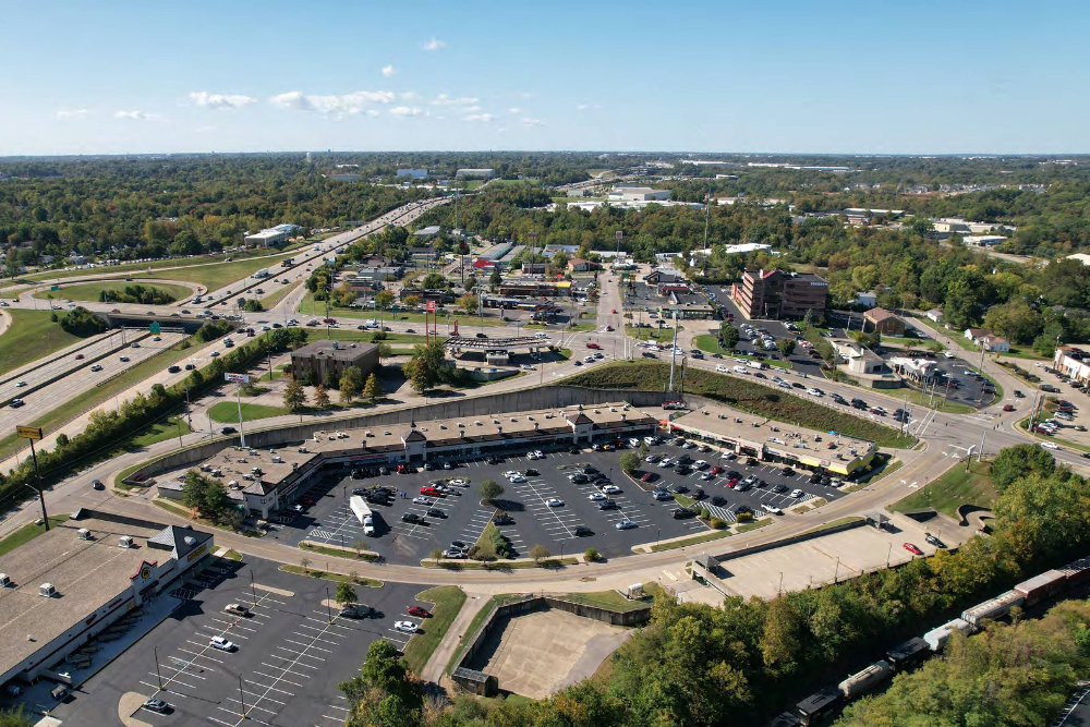 Aerial view of a large suburban shopping complex with a circular parking lot and surrounding roads.