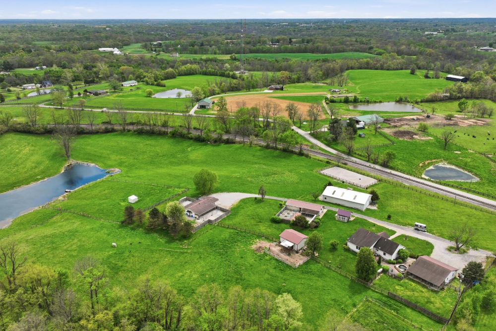 Aerial view of a rural farm landscape with green pastures, fences, and several ponds near houses along a road.