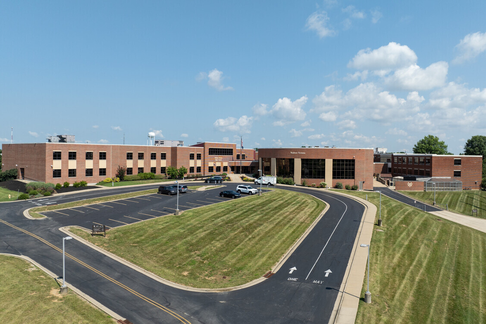 Walton-Kentucky | Helmer Somers Law Aerial view of a brick school building with a curved driveway, parking lot, and green lawns on a sunny day.